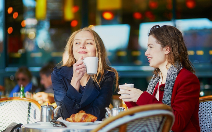 Two young girls enjoying coffee at a cafe table with croissants.