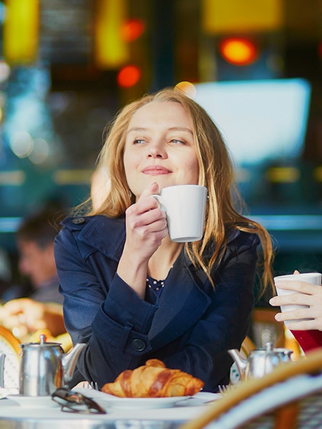 Two young girls enjoying coffee at a cafe table with croissants.