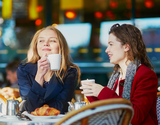 Two young girls enjoying coffee at a cafe table with croissants.