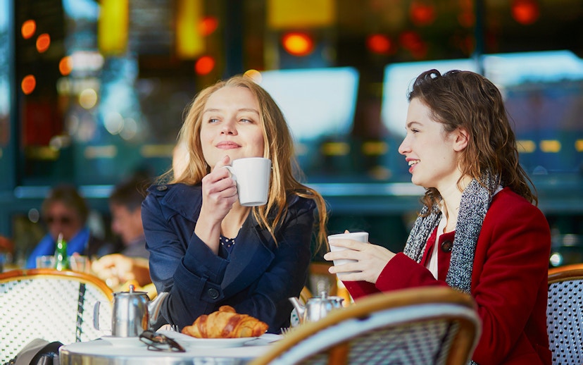 Two young girls enjoying coffee at a cafe table with croissants.