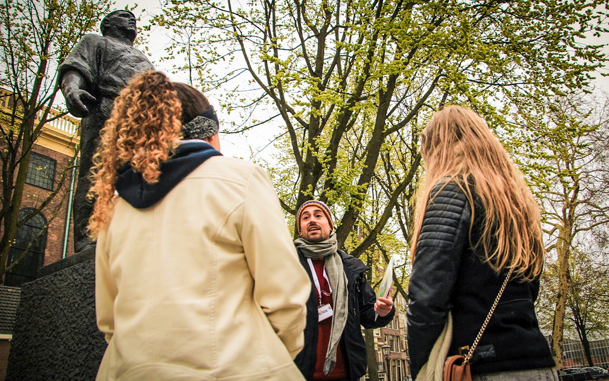 Tour guide speaking to group near statue during Amsterdam winter walking tour.