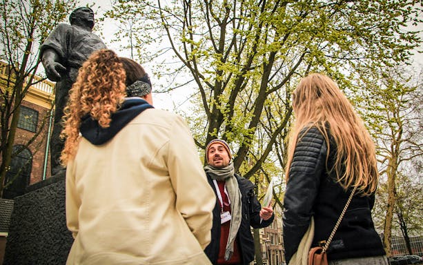 Tour guide speaking to group near statue during Amsterdam winter walking tour.