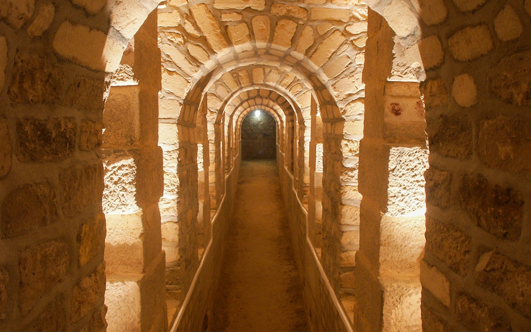 Corridor in the Paris Catacombs with stone arches and dim lighting.