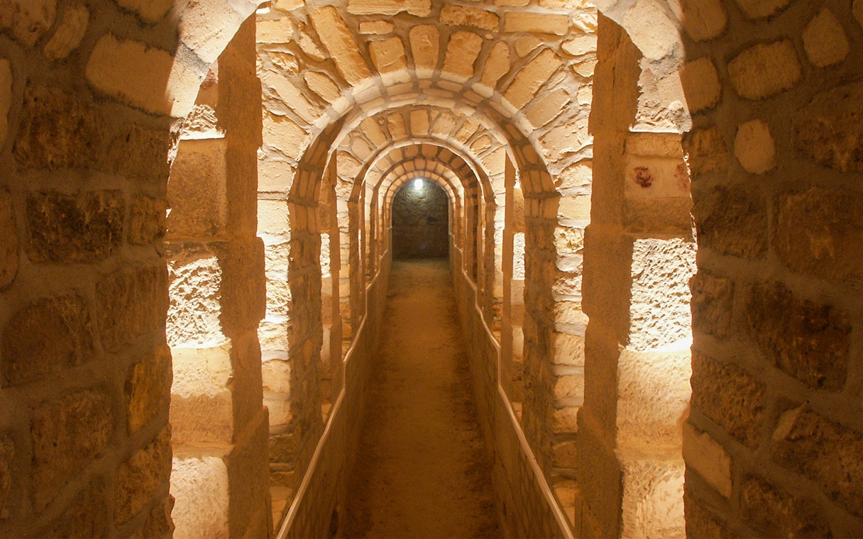 Corridor in the Paris Catacombs with stone arches and dim lighting.