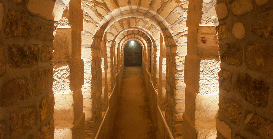Corridor in the Paris Catacombs with stone arches and dim lighting.