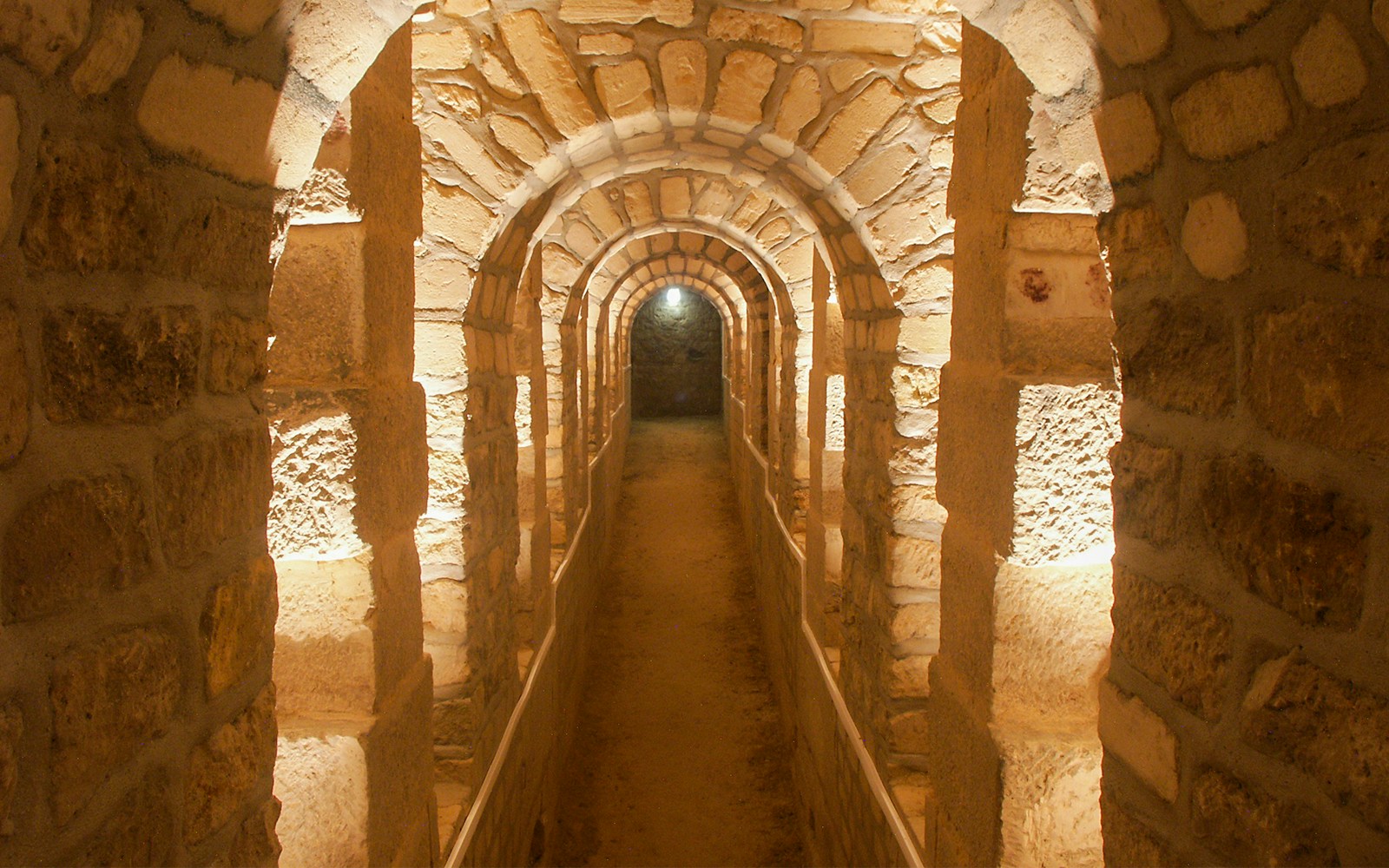 Corridor in the Paris Catacombs with stone arches and dim lighting.