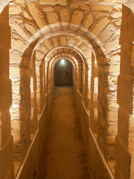 Corridor in the Paris Catacombs with stone arches and dim lighting.