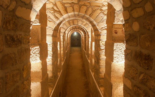 Corridor in the Paris Catacombs with stone arches and dim lighting.