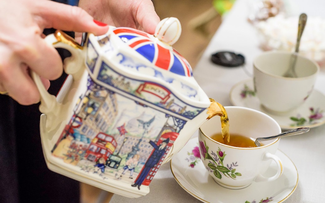 Pouring tea from a decorative teapot into a floral cup at Tate Modern Restaurant.