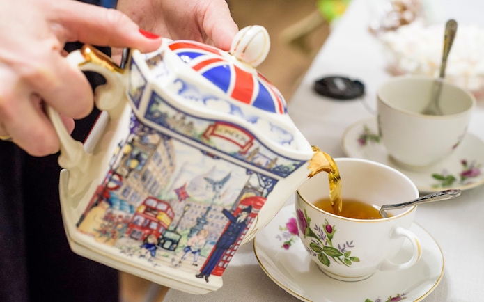 Pouring tea from a decorative teapot into a floral cup at Tate Modern Restaurant.