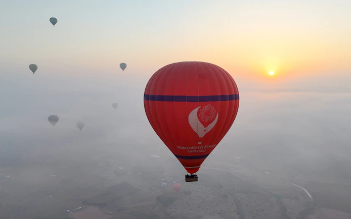 Hot air balloons floating over Marrakech at sunrise.
