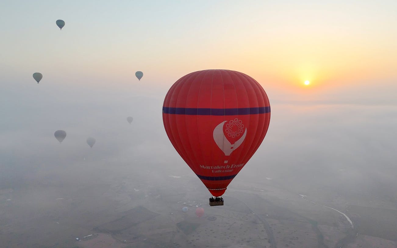 Hot air balloons floating over Marrakech at sunrise.