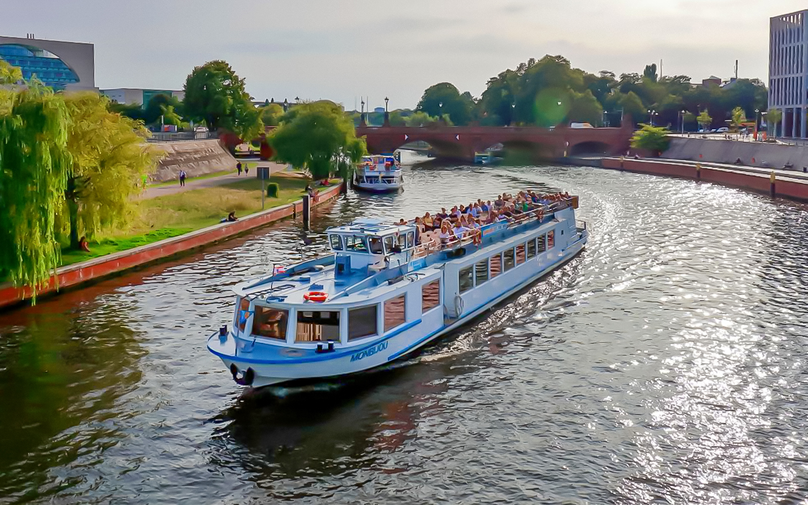Berlin sightseeing cruise boat on the Spree River passing under a bridge with passengers.