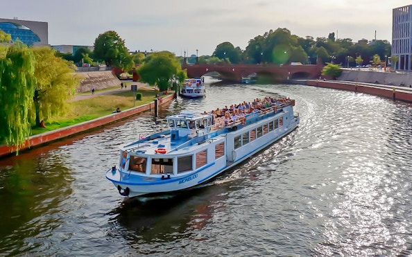 Berlin sightseeing cruise boat on the Spree River passing under a bridge with passengers.