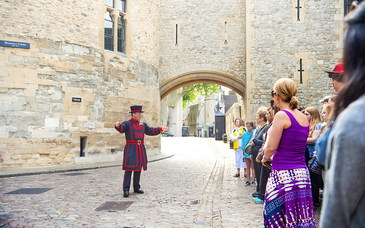 Beefeater leading a morning tour at the Tower of London with visitors gathered around.