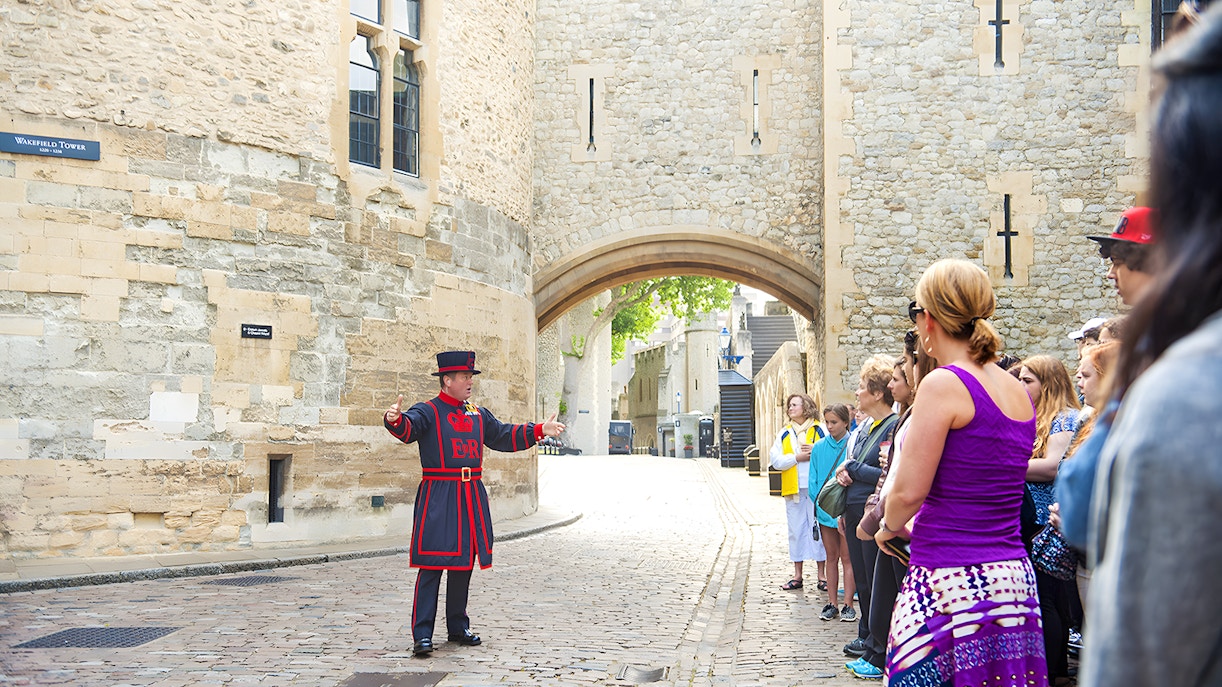 Beefeater leading a morning tour at the Tower of London with visitors gathered around.