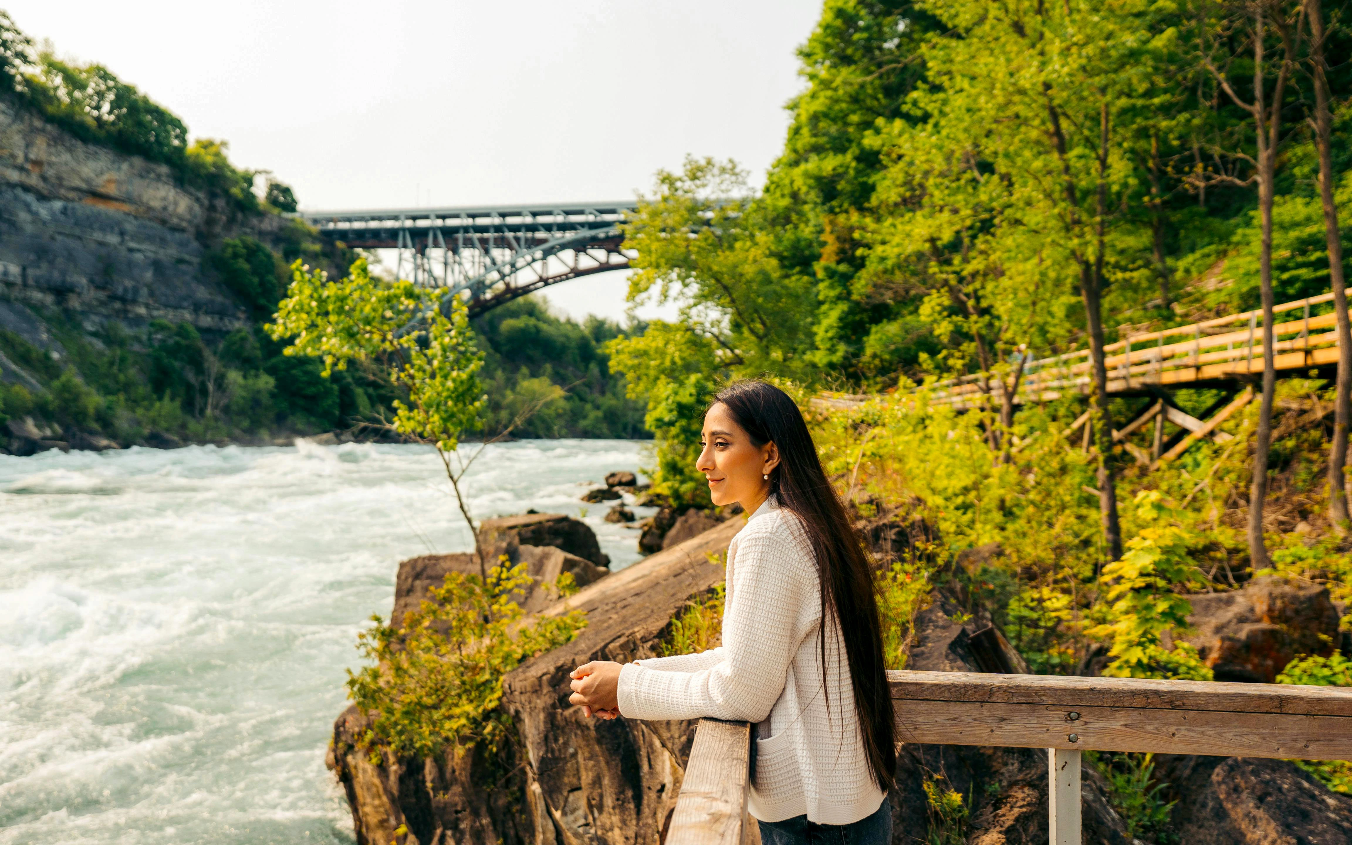 Visitor enjoying the view at White Water Walk, Niagara Parks, with river and bridge in background.