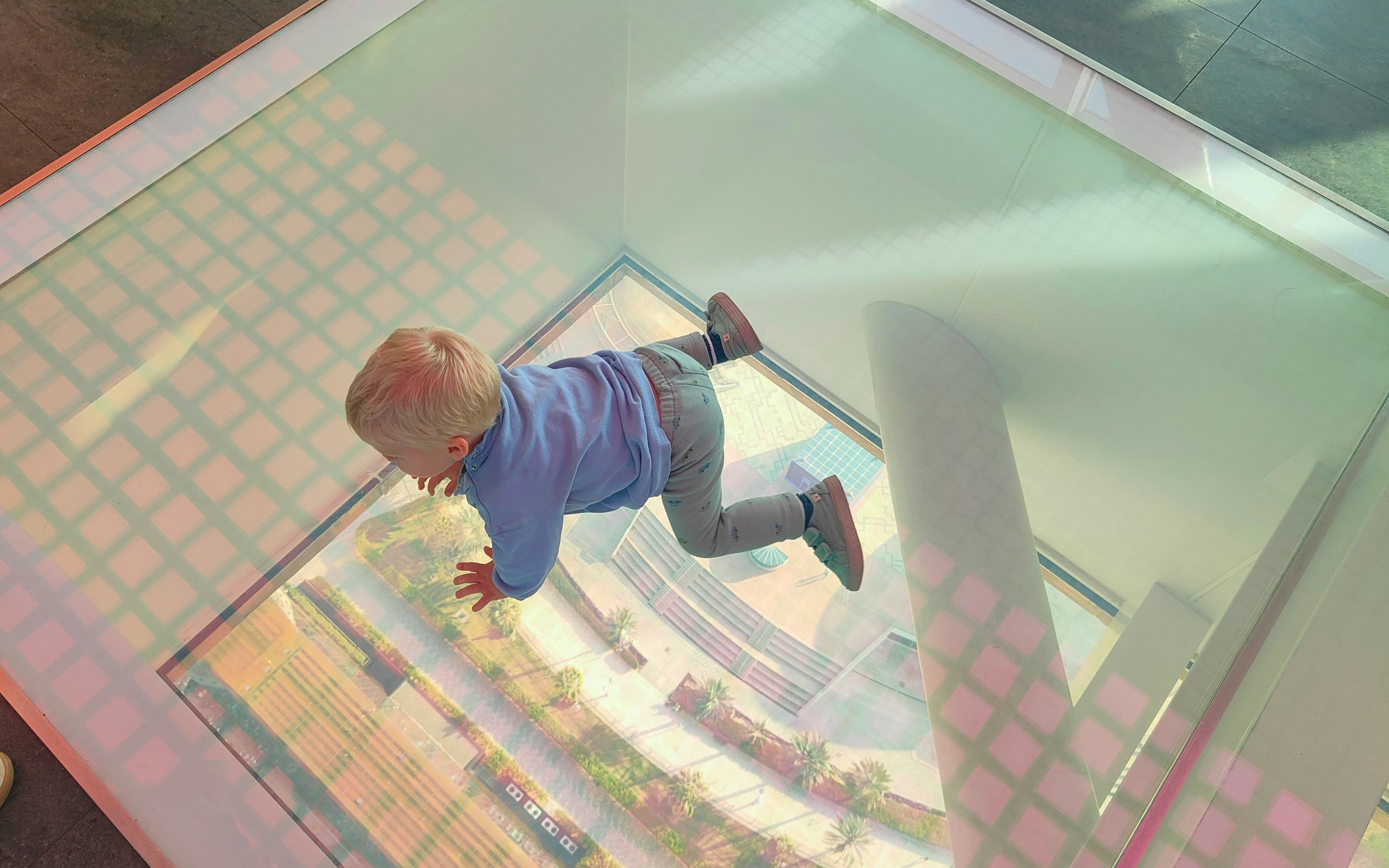 Baby crawling on glass floor at Dubai Frame with city view below.