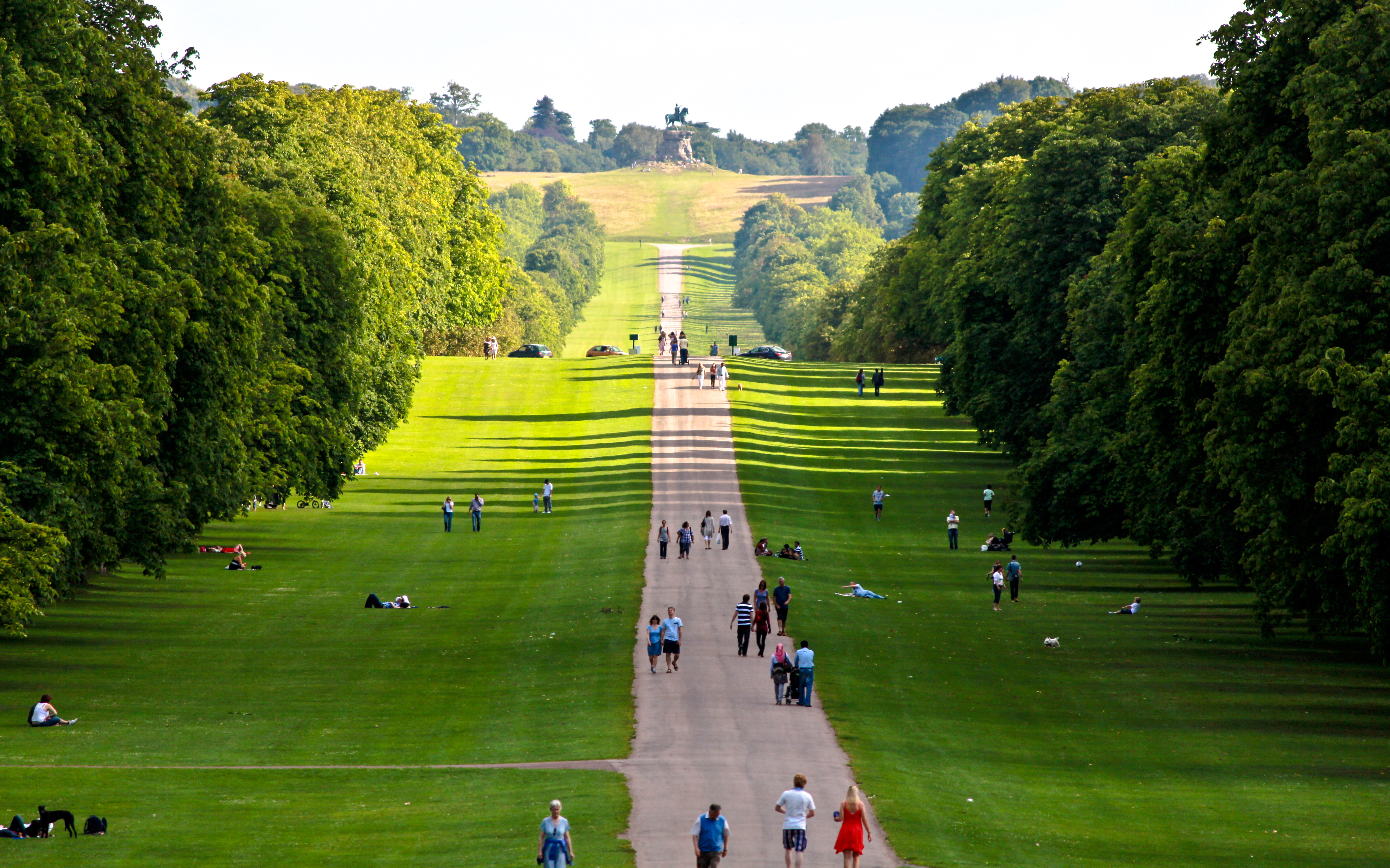 People walking along the Windsor Long Walk, surrounded by lush green trees.