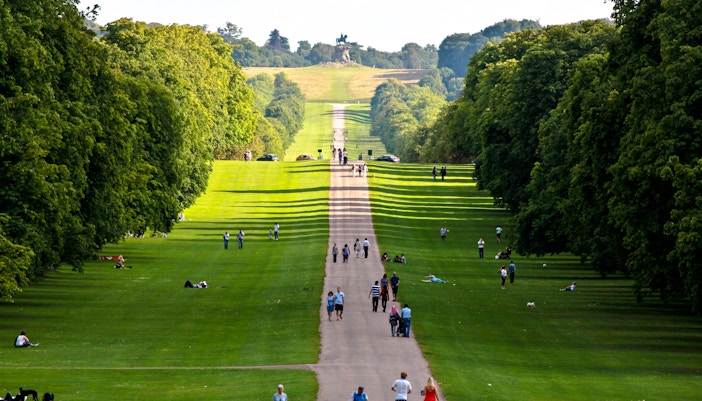 People walking along the Windsor Long Walk, surrounded by lush green trees.