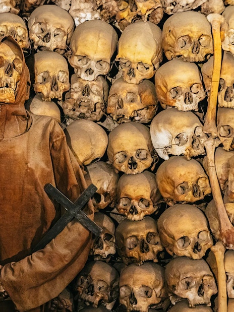 Skeleton in robe surrounded by skulls in Roman catacombs on the Appian Way.