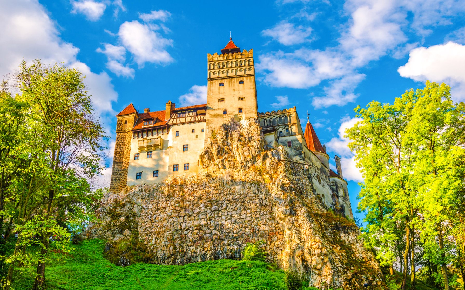 Bran Castle in Romania surrounded by lush greenery and a clear blue sky.
