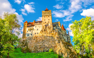 Bran Castle in Romania surrounded by lush greenery and a clear blue sky.
