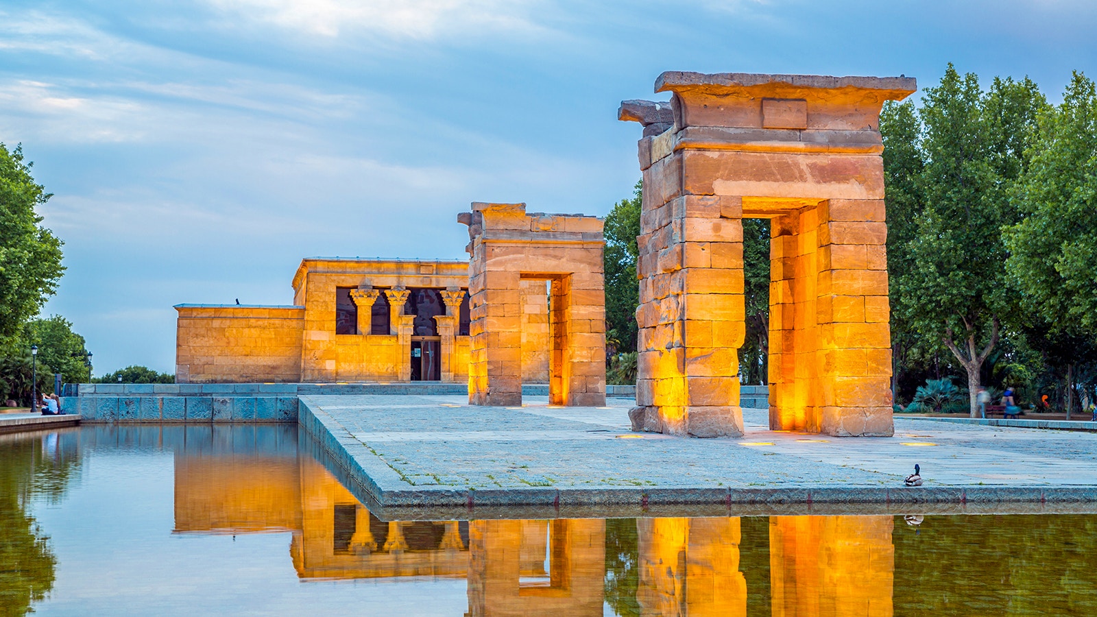 Temple of Debod in Madrid at sunset with illuminated ancient Egyptian structures reflected in water.