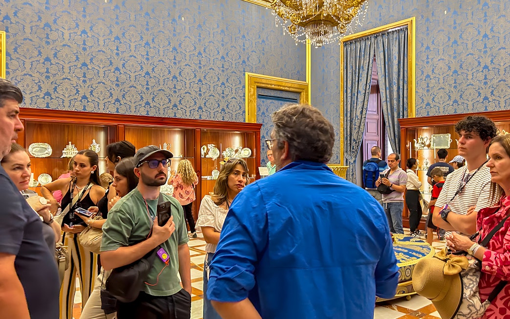 Visitors on a guided tour inside the Royal Palace of Madrid, viewing ornate displays.