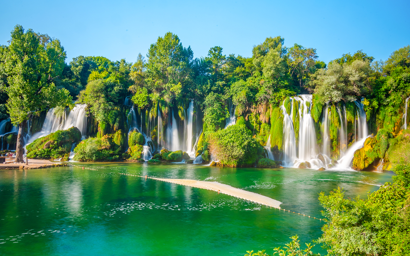 Kravica waterfall cascading into a turquoise pool surrounded by lush greenery in Bosnia and Herzegovina.