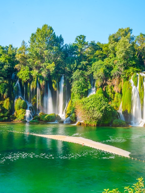 Kravica waterfall cascading into a turquoise pool surrounded by lush greenery in Bosnia and Herzegovina.