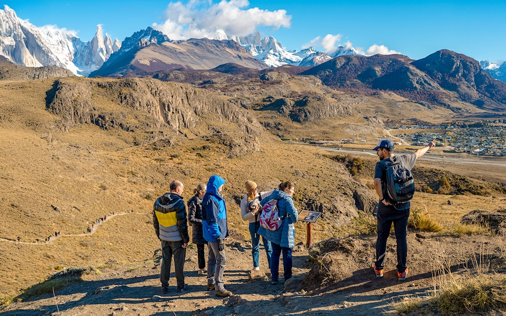Tourists on a hiking trail in El Chaltén, Argentina, with mountains in the background.