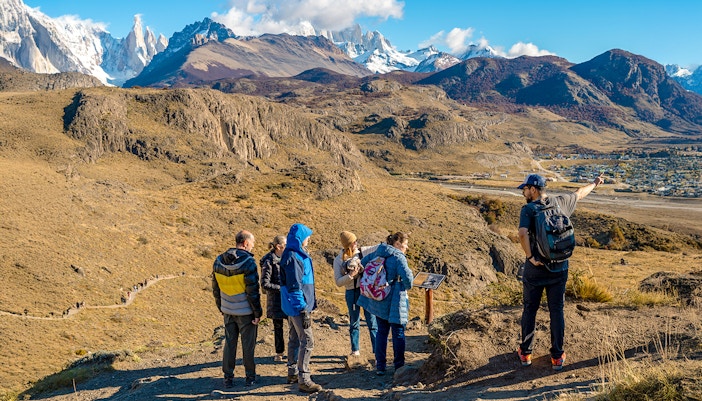 Tourists on a hiking trail in El Chaltén, Argentina, with mountains in the background.