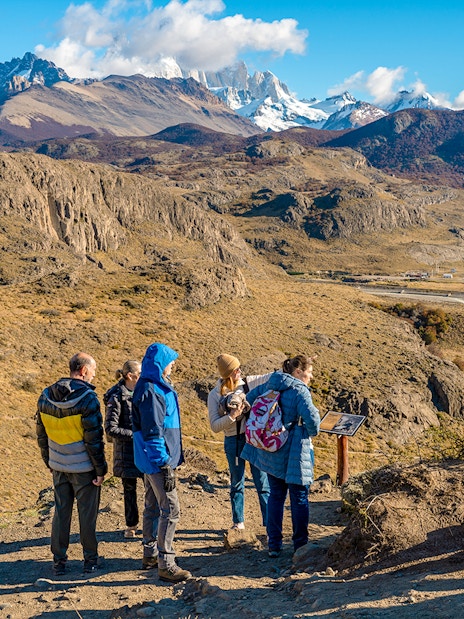 Tourists on a hiking trail in El Chaltén, Argentina, with mountains in the background.