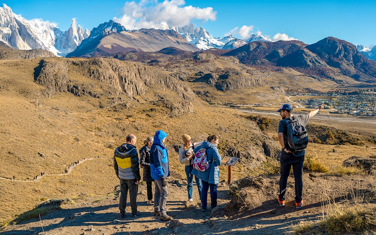 Tourists on a hiking trail in El Chaltén, Argentina, with mountains in the background.