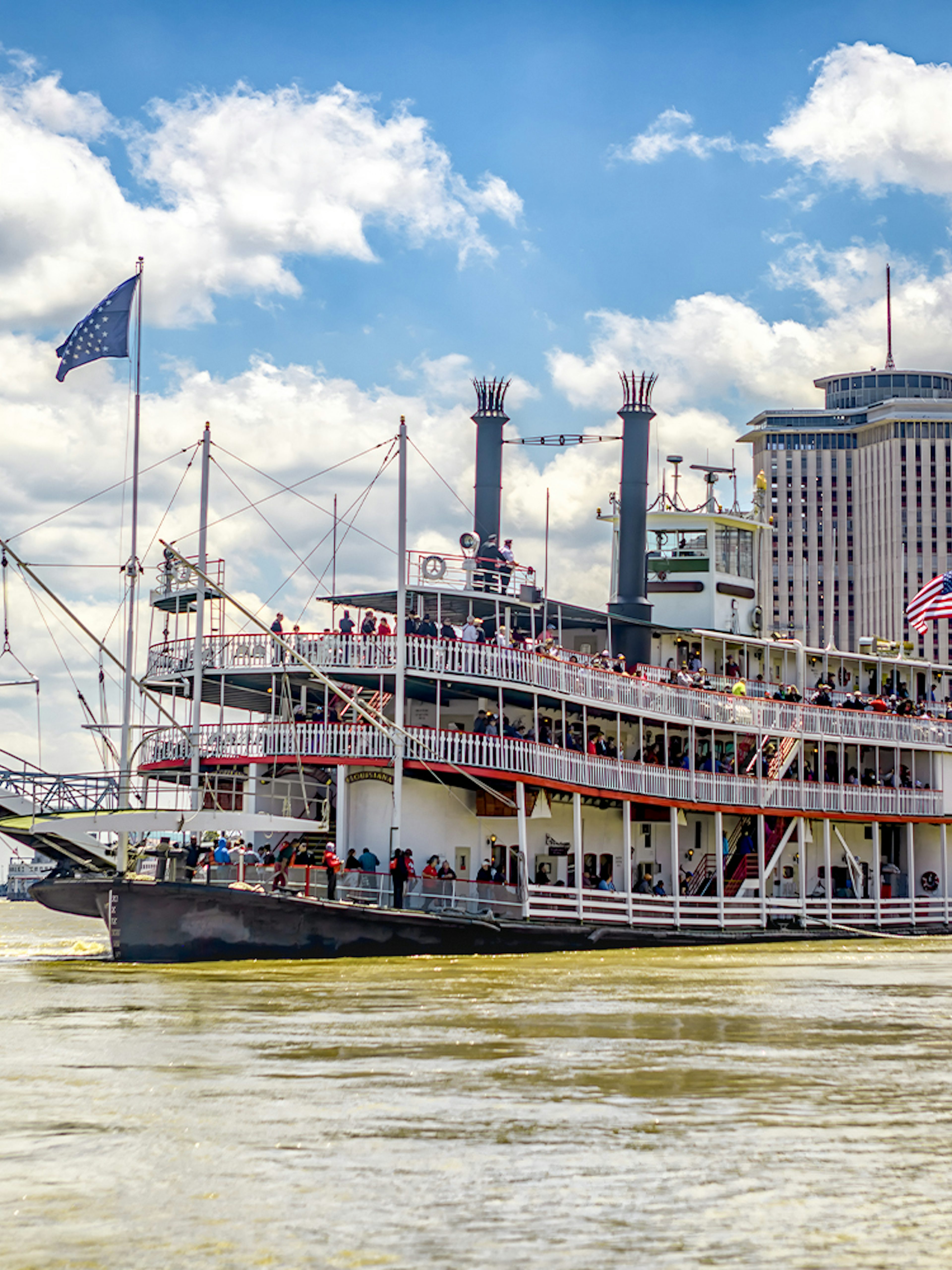Steamboat Natchez cruising on the Mississippi River in New Orleans, Louisiana, with city skyline and bridge in view.