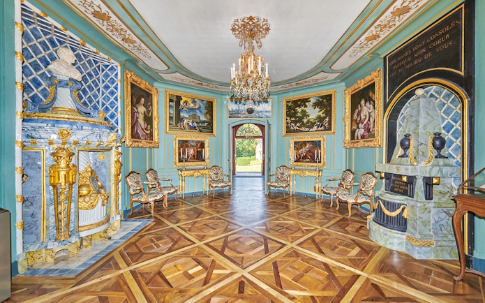 Voltaire's castle interior with ornate decor and paintings, showcasing elegant furnishings.
