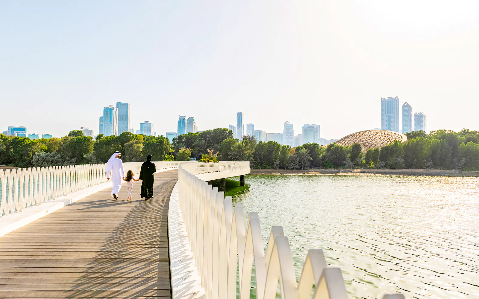 Family walking on Al Noor Island bridge with Sharjah skyline in the background.