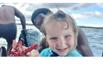 Child holding a starfish on a boat during Zanzibar day trip from Dar es Salaam.
