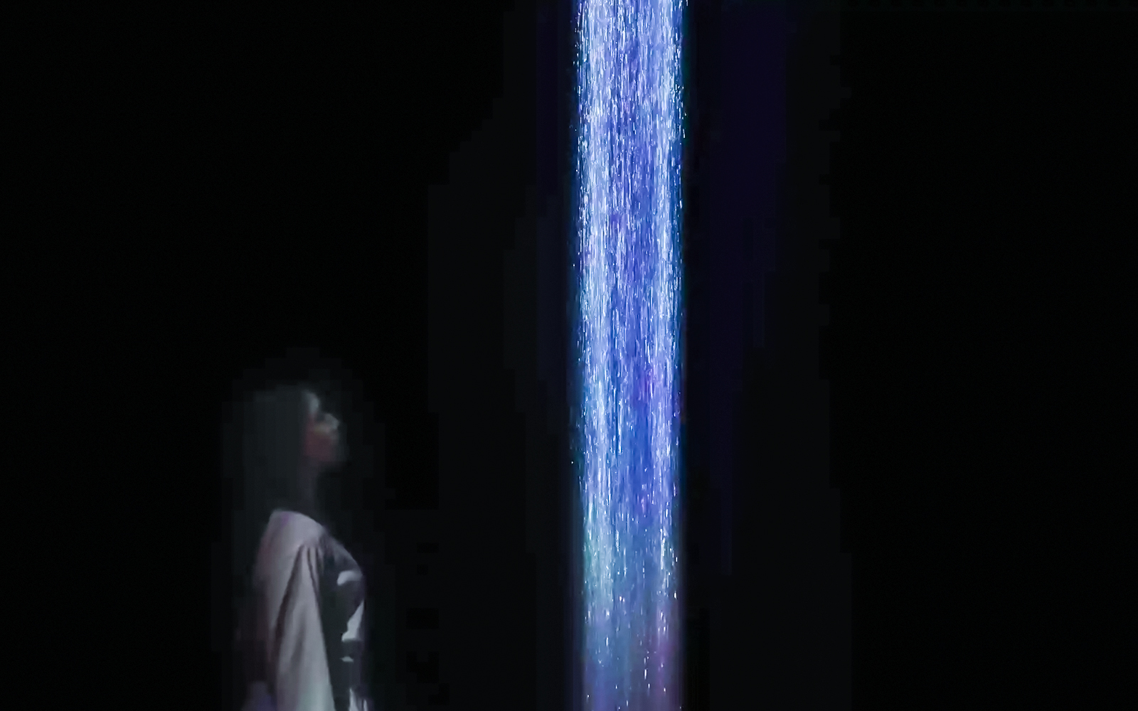 Person observing digital waterfall at teamLabs exhibition.
