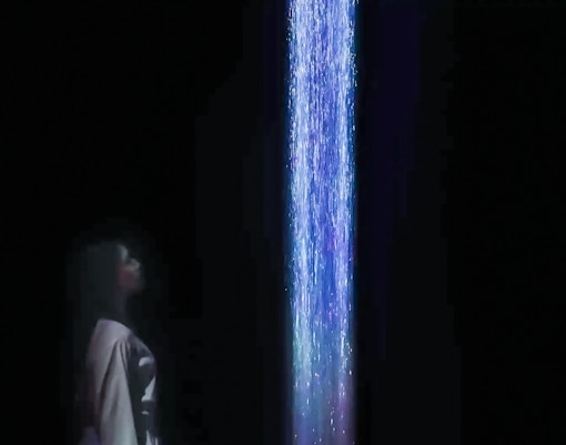 Person observing digital waterfall at teamLabs exhibition.