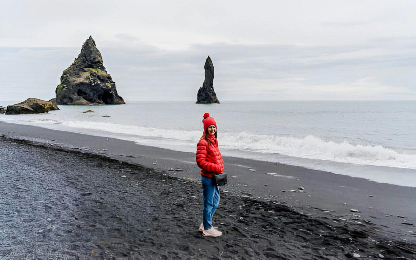 Guest walking on Reynisfjara black sand beach with sea stacks in Iceland.