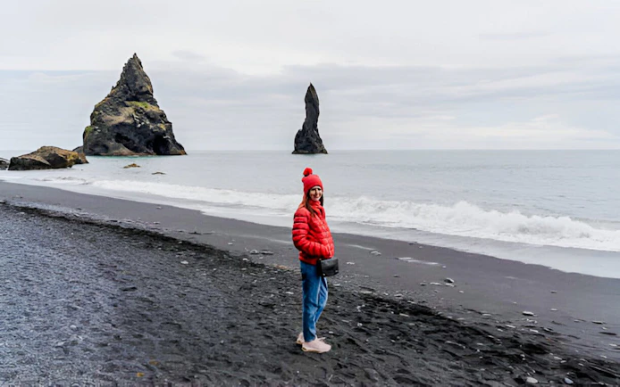Guest walking on Reynisfjara black sand beach with sea stacks in Iceland.