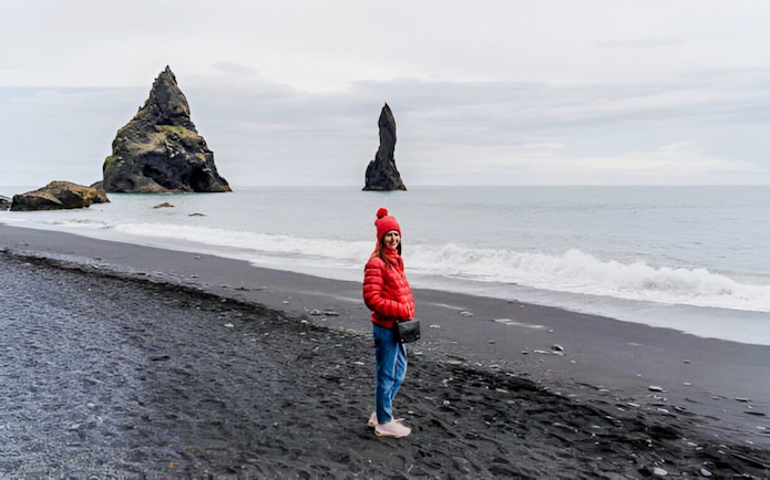 Guest walking on Reynisfjara black sand beach with sea stacks in Iceland.