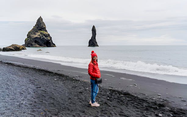 Guest walking on Reynisfjara black sand beach with sea stacks in Iceland.