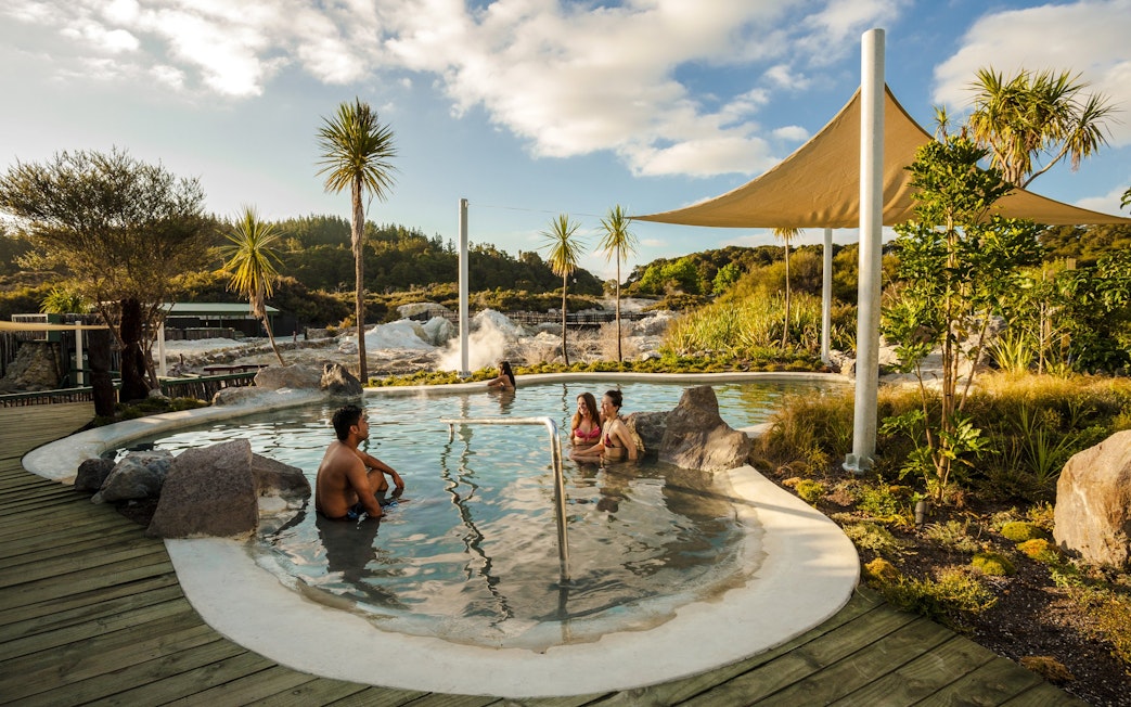 Visitors enjoying geothermal mud bath at Hell's Gate, surrounded by lush greenery and steam.