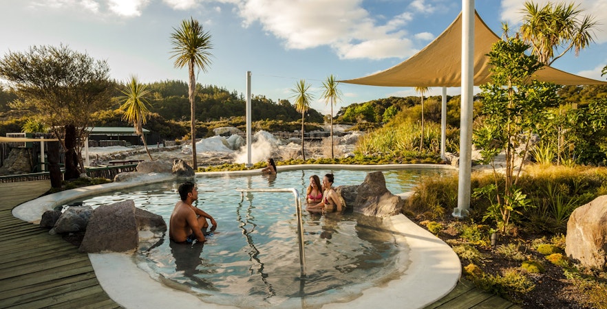 Visitors enjoying geothermal mud bath at Hell's Gate, surrounded by lush greenery and steam.