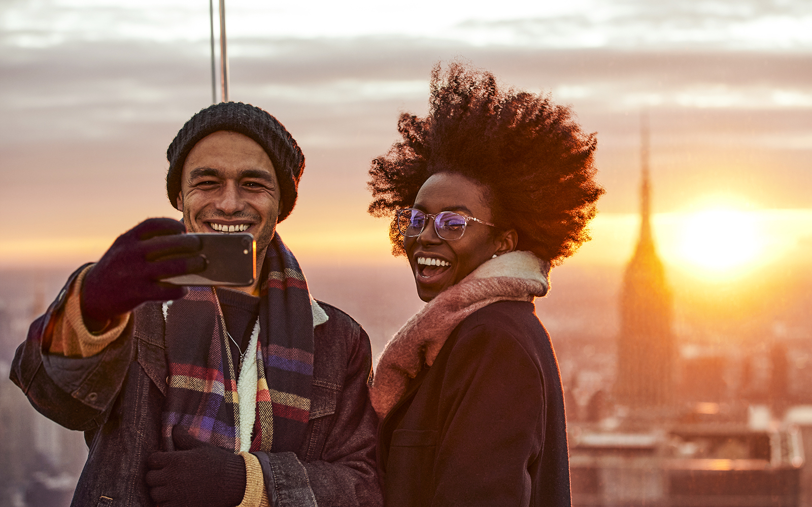 Couple taking a selfie on the Sky Deck with city skyline at sunset.