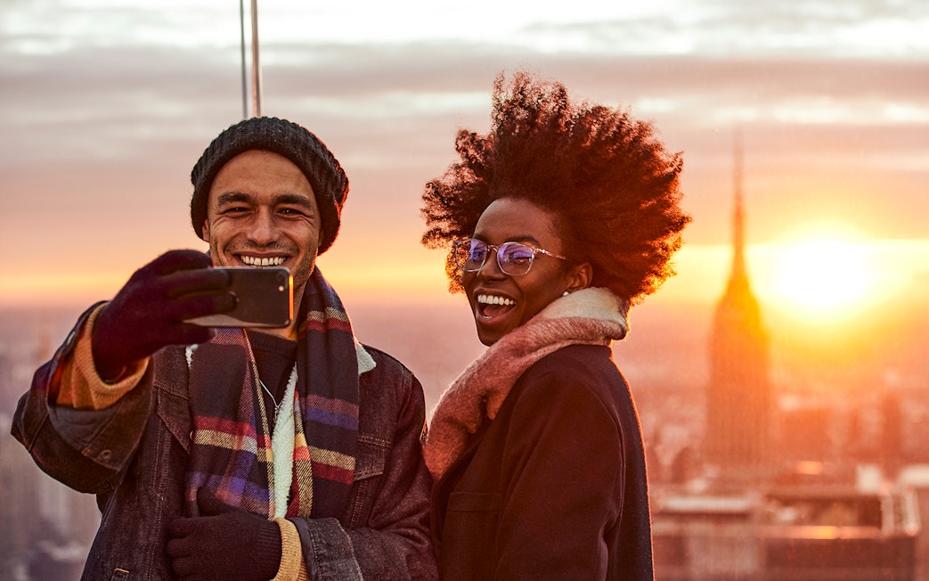 Couple taking a selfie on the Sky Deck with city skyline at sunset.