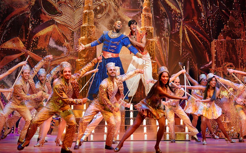 Performers in vibrant costumes on stage during an Aladdin musical show.